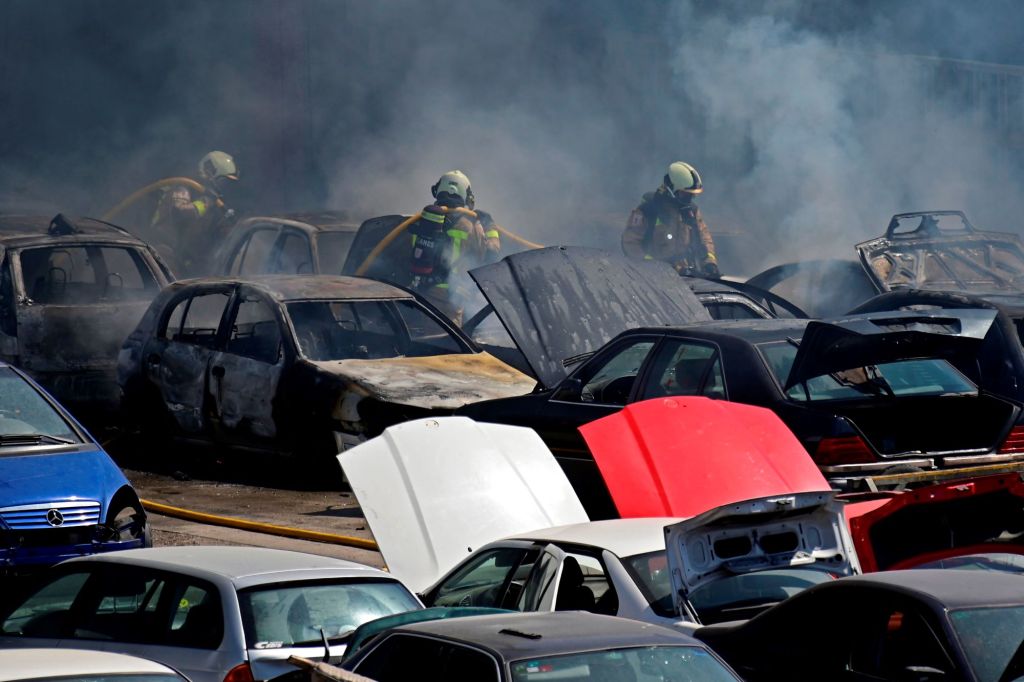 A depiction of a junkyard fire with firefighters and cars.