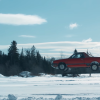 A red 1984 Subaru Brat coupe utility jumps over a frozen lake in Vermont with Travis Pastrana behind the wheel.