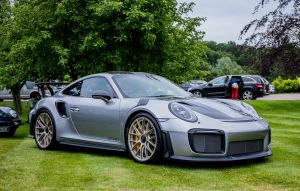 A silver and black Porsche 911 GT2 RS in front of a wooded area parked on grass. 