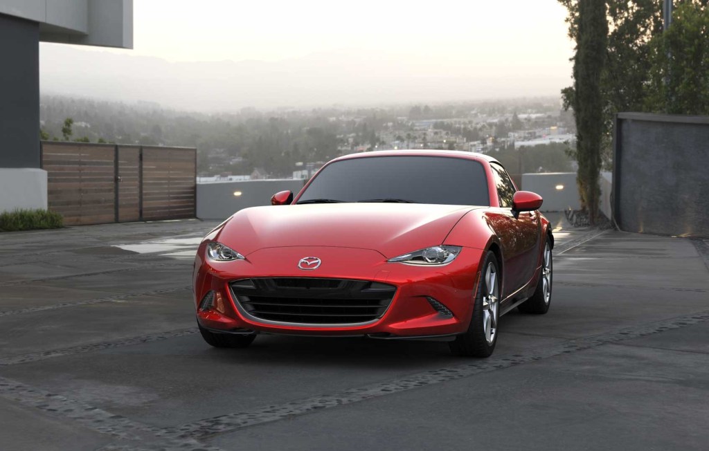 Red 2022 Mazda MX-5 Miata, a car with high gas mileage and fast acceleration, parked by a large house