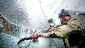 A man scrapes ice off the windshield of a car, an ice scraper is just one of our tips for driving in winter weather.