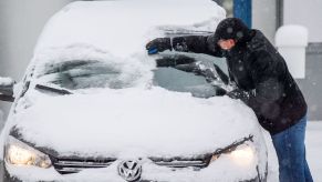 Snow on a car with a person cleaning it off. if only they had the best new car features for winter driving