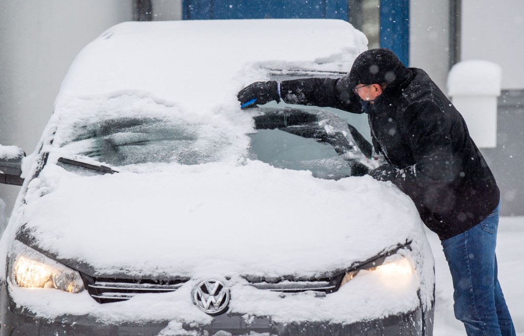 Snow on a car with a person cleaning it off. if only they had the best new car features for winter driving
