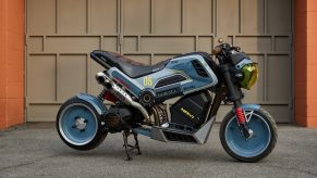 The blue-black-and-yellow Steady Garage 'Project Naviscape' custom 2022 Honda Navi next to a garage