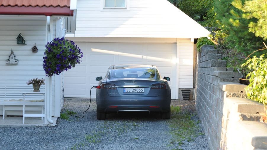 A grey Tesla charging in front a white residential home.