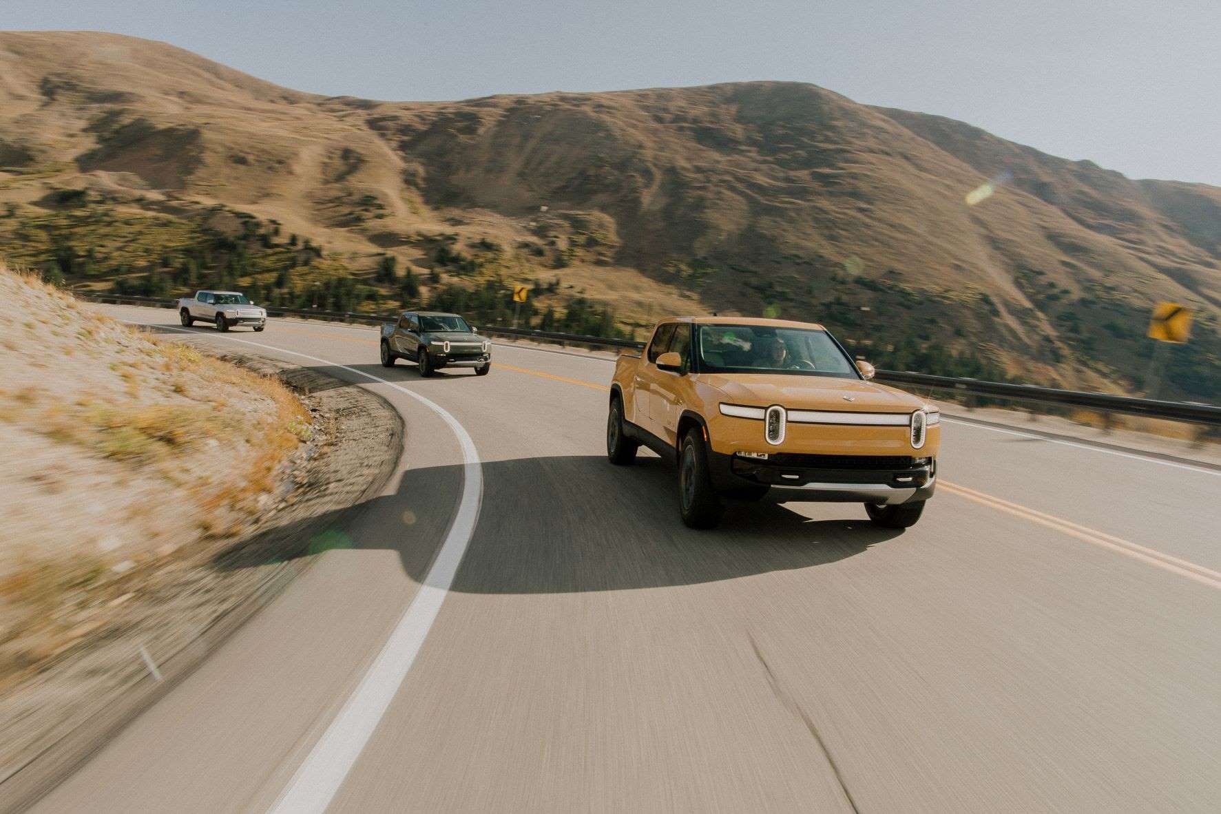 Three 2022 Rivian R1T electric pickup trucks driving on a mountain road