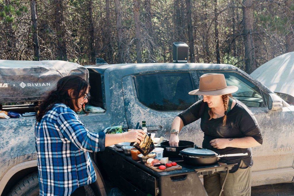 Two women cooking with the 2022 Rivian R1T camp kitchen while on an off-road adventure
