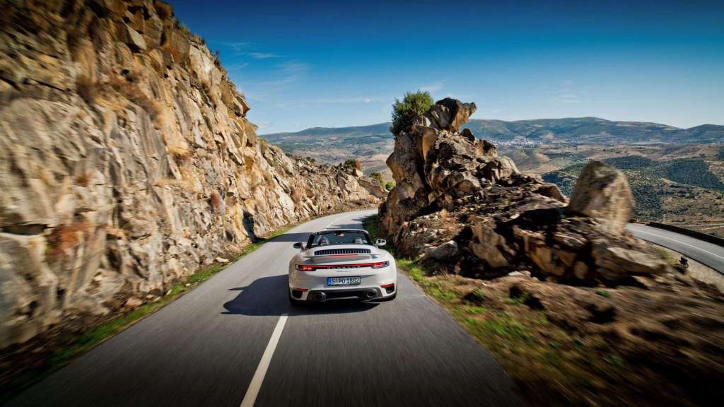White fully loaded new 2022 Porsche 911 Turbo S Cabriolet convertible driving on a winding mountain road