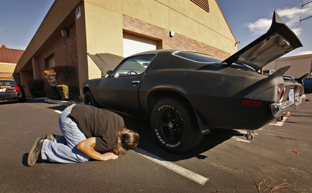 A potential buyer checks the underside of a Chevy Camaro.