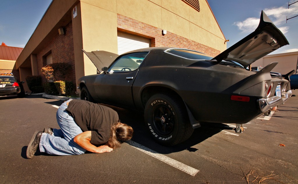 A potential buyer checks the underside of a Chevy Camaro.