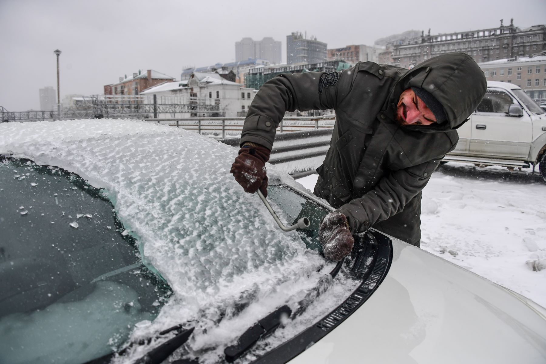 A man scraping ice off his windshield in Vladivostok, Russia