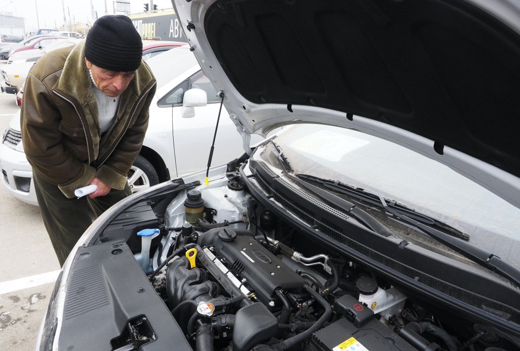 A potential car buyer checks out a car's engine bay. 