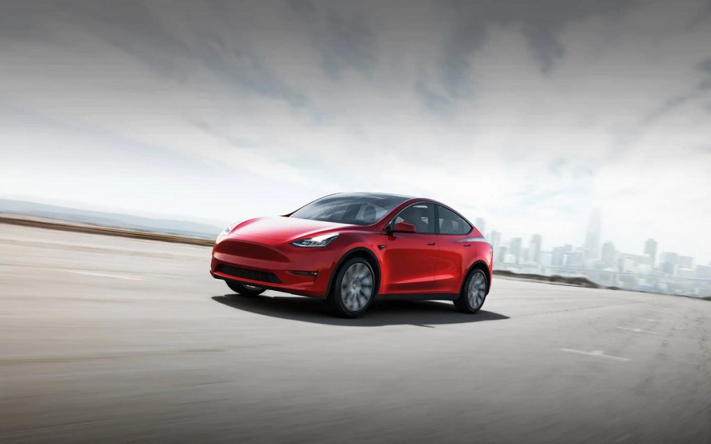 A red 2021 Tesla Model Y driving down a road, it has a longer EPA-estimated driving range than the new 2022 Kia EV6 crossover.