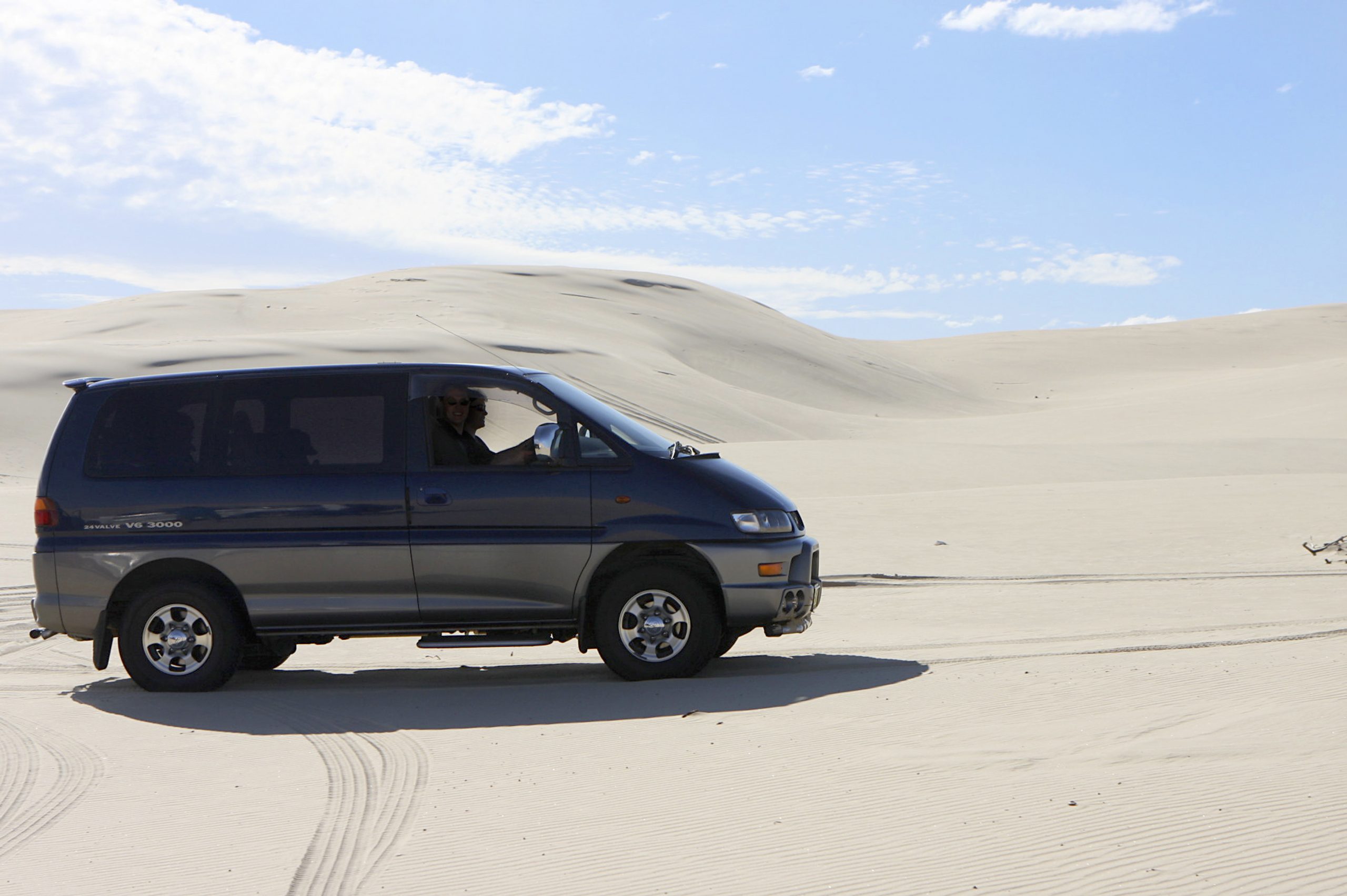 A green and gold JDM Mitsubishi Delica van shot in profile in the desert