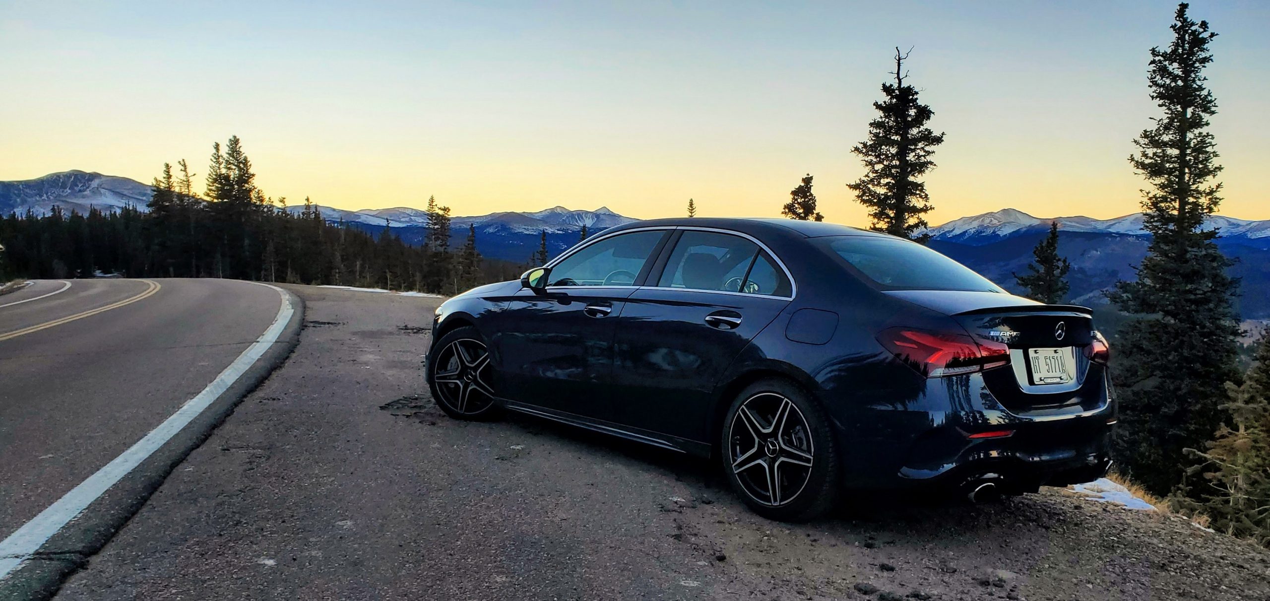 A Denim Blue 2021 Mercedes-Benz AMG A35 sedan shot from the rear 3/4 on a mountain pass at sunset