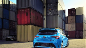 A rear 3/4 shot of a Toyota Corolla hides the new Toyota GR Corolla hot hatch in a camo livery among shipping containers