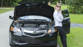 Young woman with car broken down on side of road using cell phone
