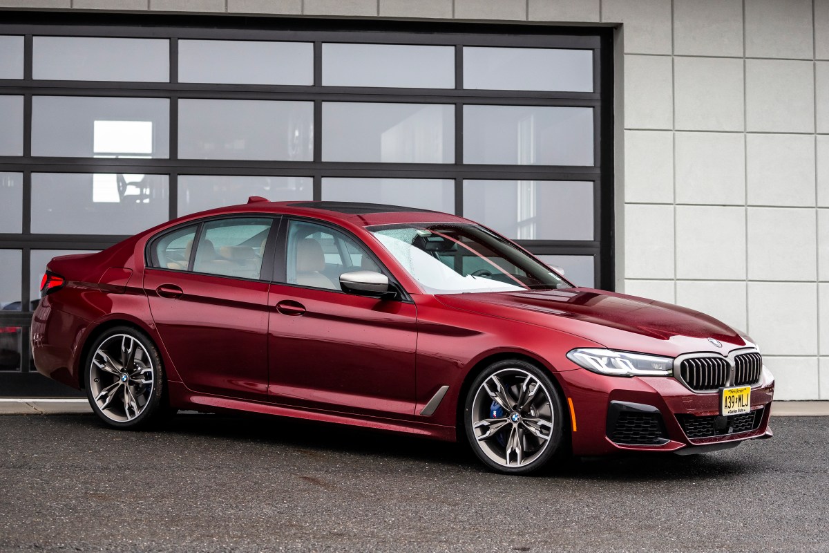 A red BMW M550i xDrive 3/4 front view while parked in a driveway.