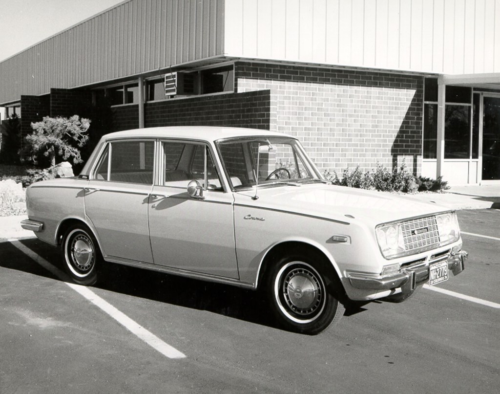 A white 1966 Toyota Corona sedan in front of a building