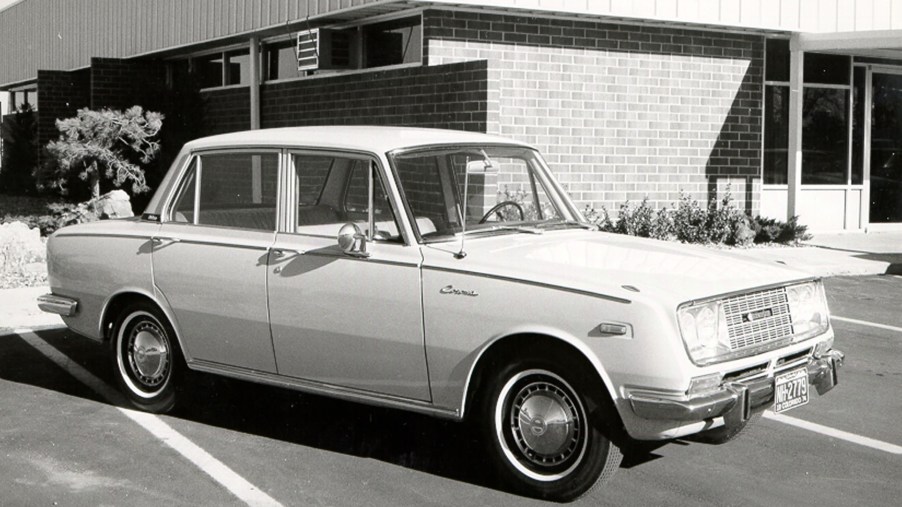A white 1966 Toyota Corona sedan in front of a building