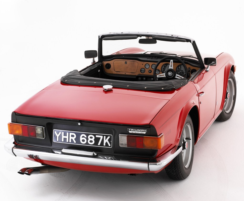 The overhead rear 3/4 view of a red 1972 Triumph TR6 with a black-vinyl interior and wood dashboard