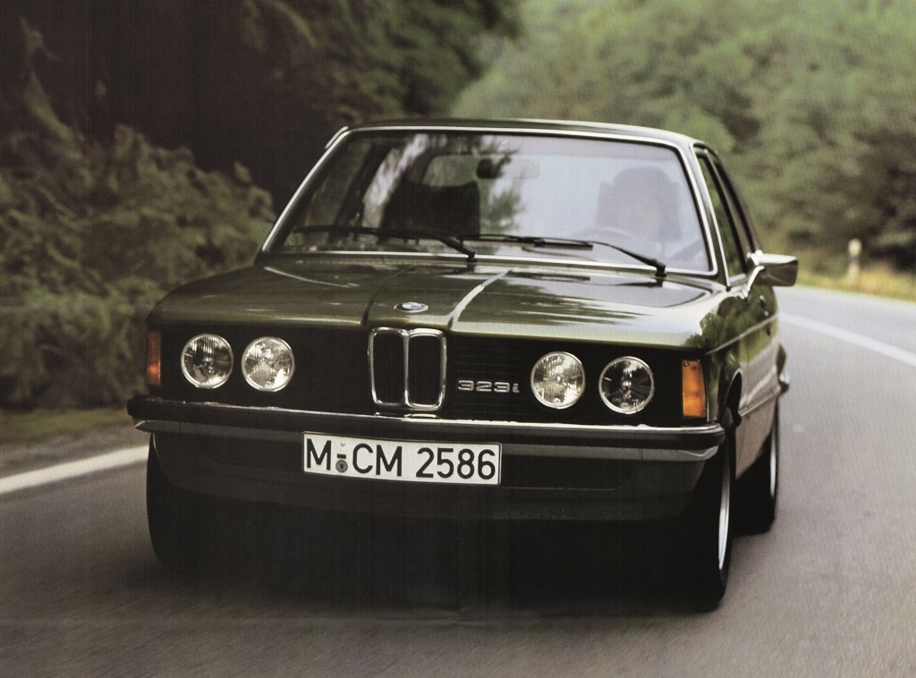 A green 1979 E30 BMW 323i drives down a forest road