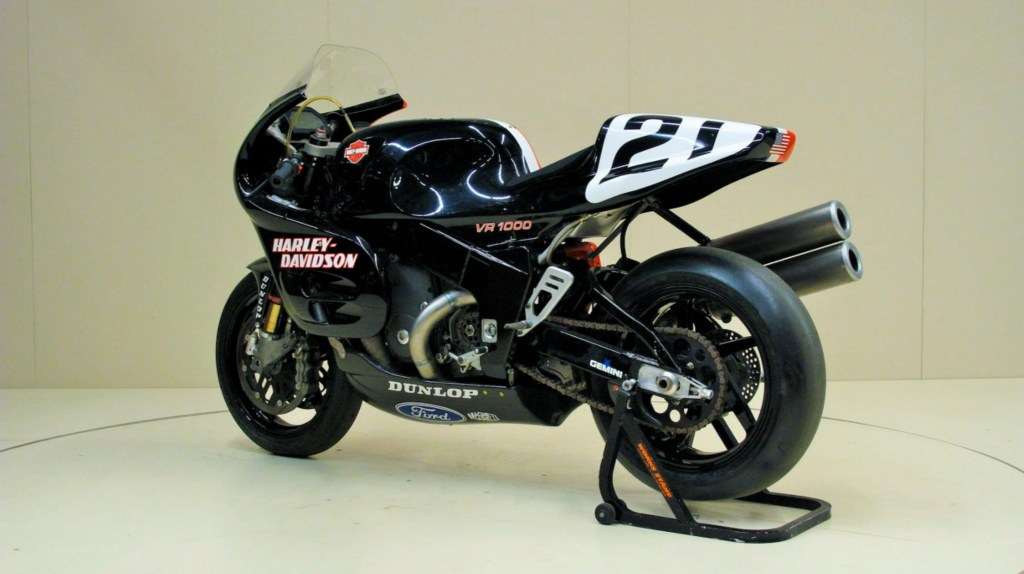 The left rear 3/4 view of a black-and-orange 1994 Harley-Davidson VR1000 on a rear-wheel stand