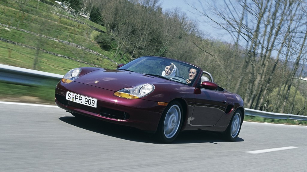 A purple 1996 986 Porsche Boxster convertible sports car drives down a road