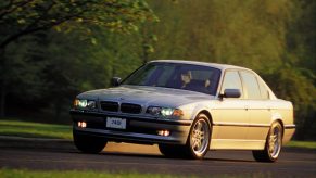 A silver 2001 E38 BMW 740i Sport driving down a forest road
