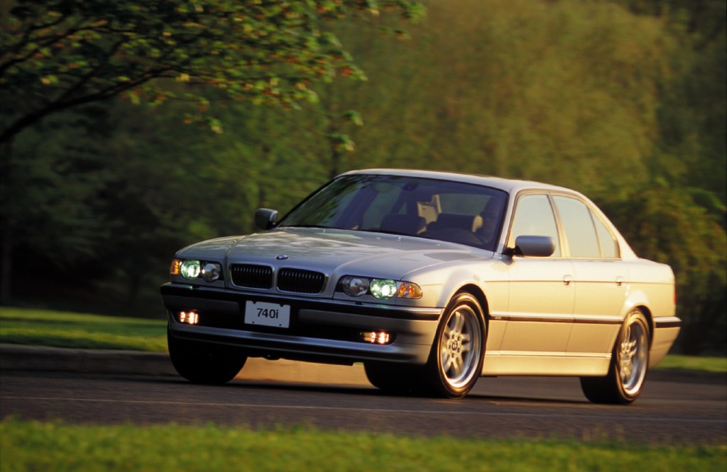 A silver 2001 E38 BMW 740i Sport driving down a forest road