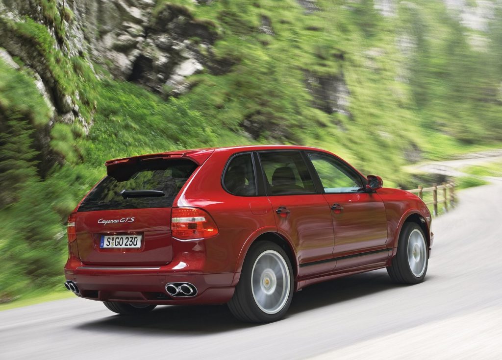 The rear 3/4 view of a red 2008 Porsche Cayenne GTS driving on a mountain road