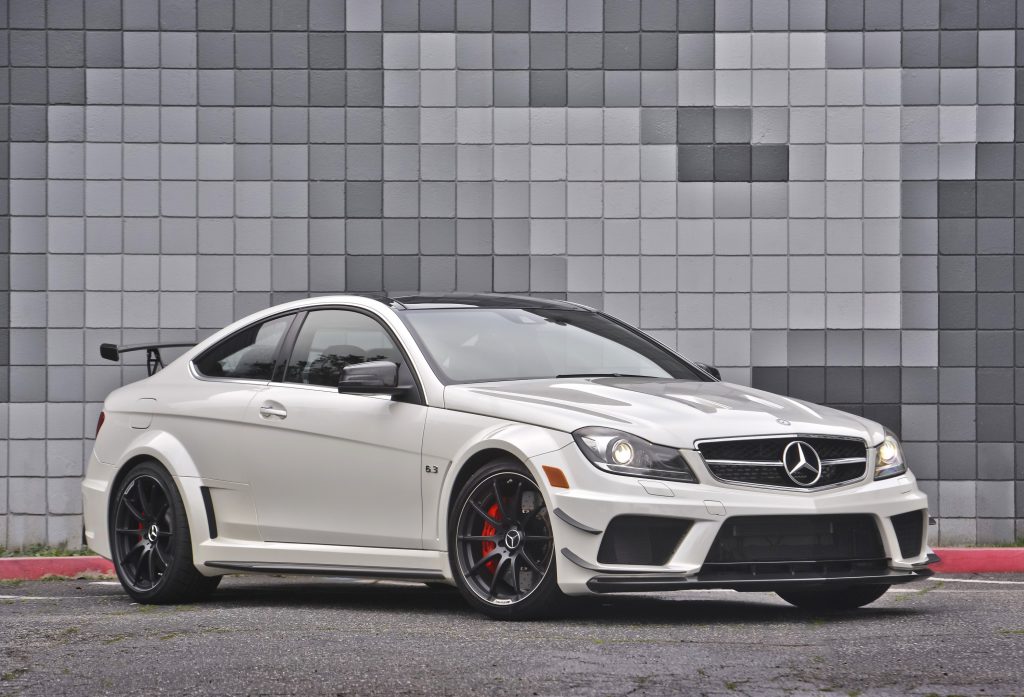 A white 2012 W204 Mercedes C63 AMG Black Series against a gray-brick background