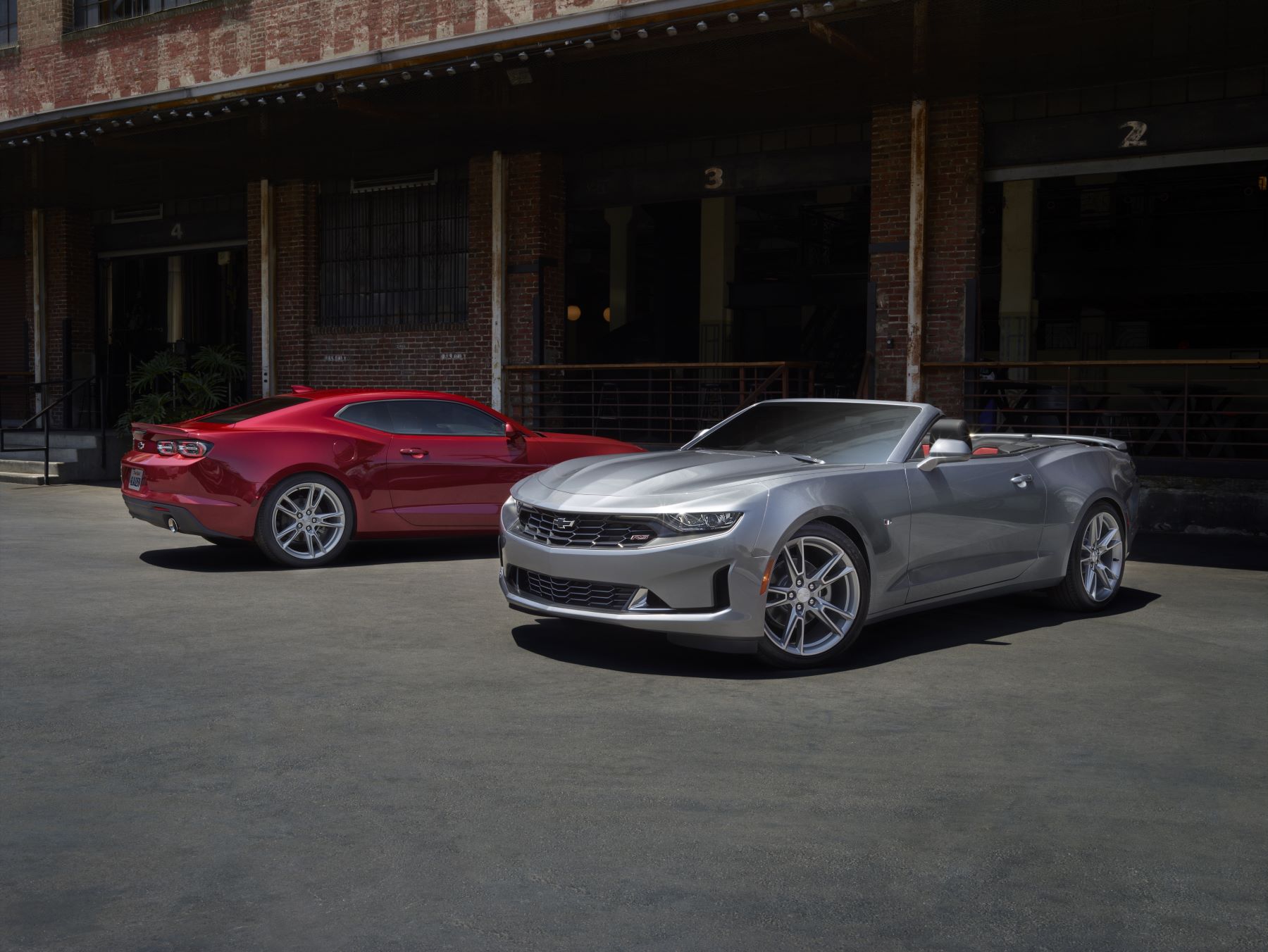 2021 Chevrolet Camaro LS and LT muscle car models in red and silver parked outside of a brick building