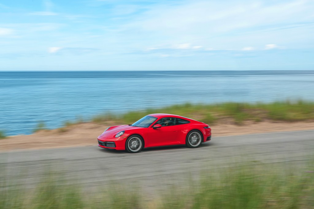 A red 2021 Porsche 911 Carrera drives by a body of water