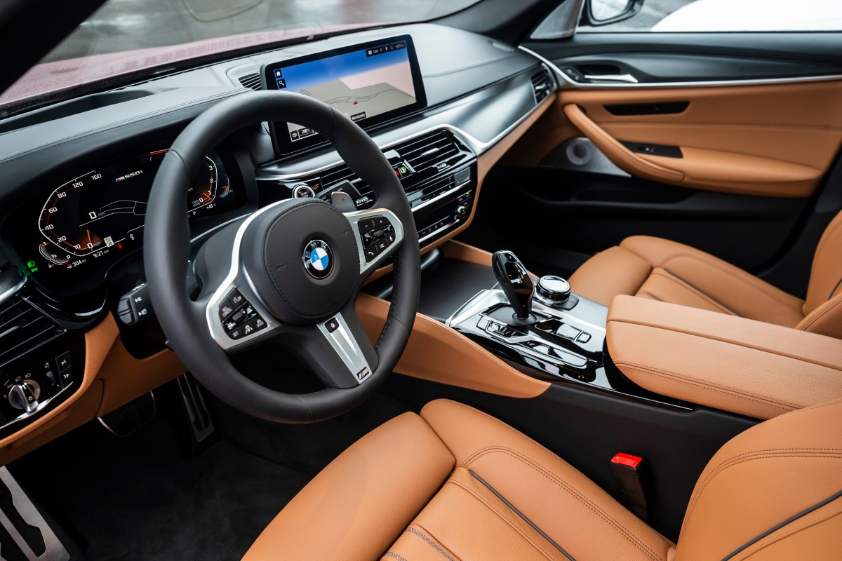A view of the interior of a BMW M550i xDrive sedan. Image shows driver and passenger seats, dashboard, and steering wheel. 