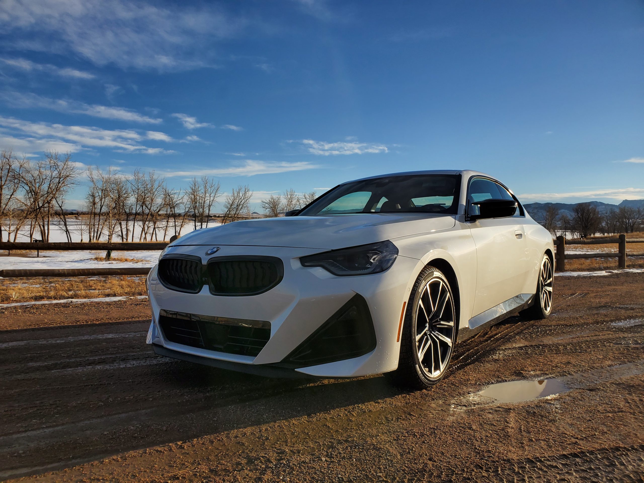 A white 2022 BMW M240i xDrive shot from the front 3/4 on a dirt road