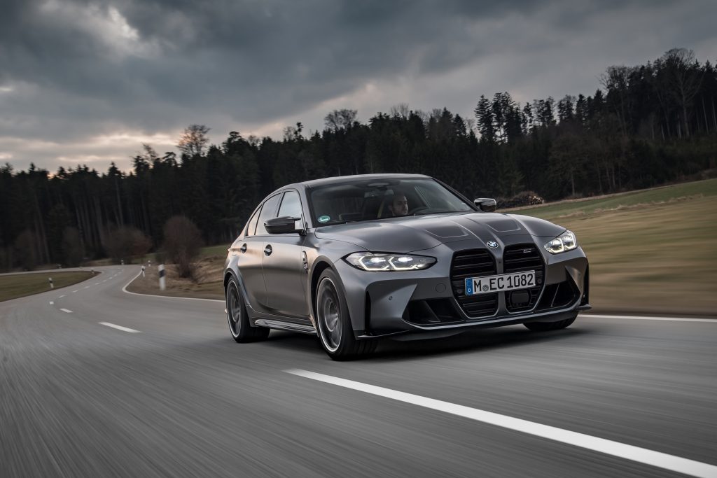 A gray 2022 BMW M3 Competition xDrive driving down a road