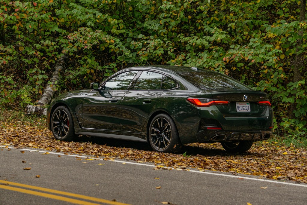 The rear 3/4 view of a green 2022 BMW M440i xDrive Gran Coupe in a forest