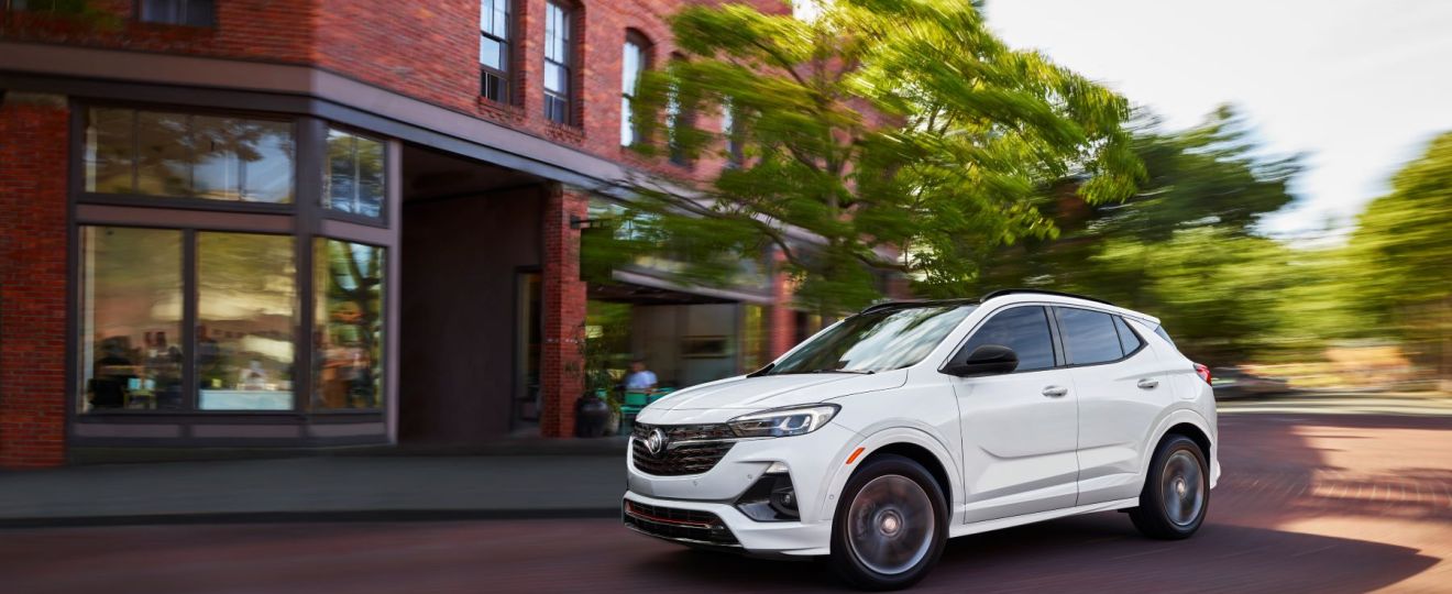 The 2022 Buick Encore GX compact crossover SUV with a white paint color option driving on a cobblestone road
