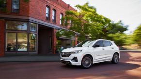 The 2022 Buick Encore GX compact crossover SUV with a white paint color option driving on a cobblestone road