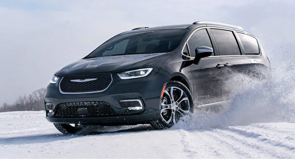 A black 2022 Chrysler Pacifica is driving in snow, there are a few reasons to buy a minivan in 2022.