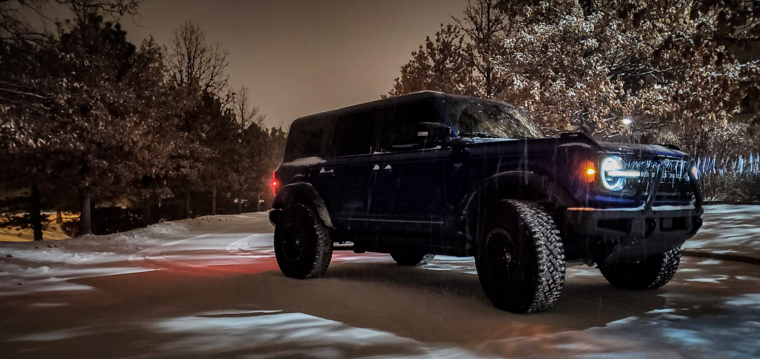A blue Bronco shot from the front 3/4 at night during a snow storm
