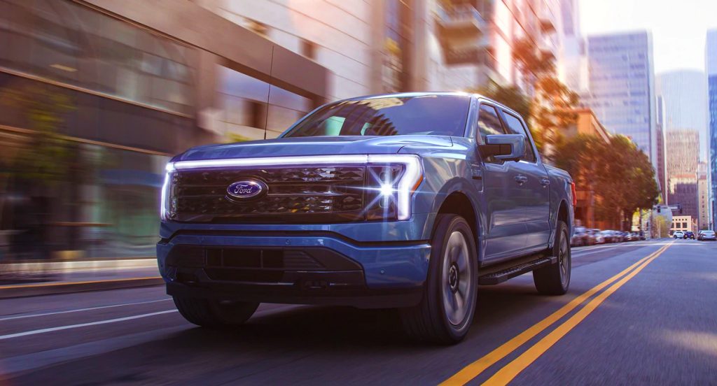 A blue 2022 Ford F-150 Lightning is driving on the road.