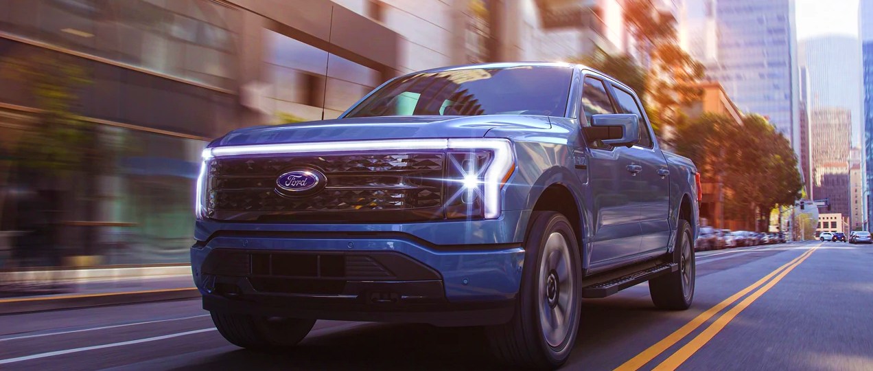 A blue 2022 Ford F-150 Lightning is driving on the road.