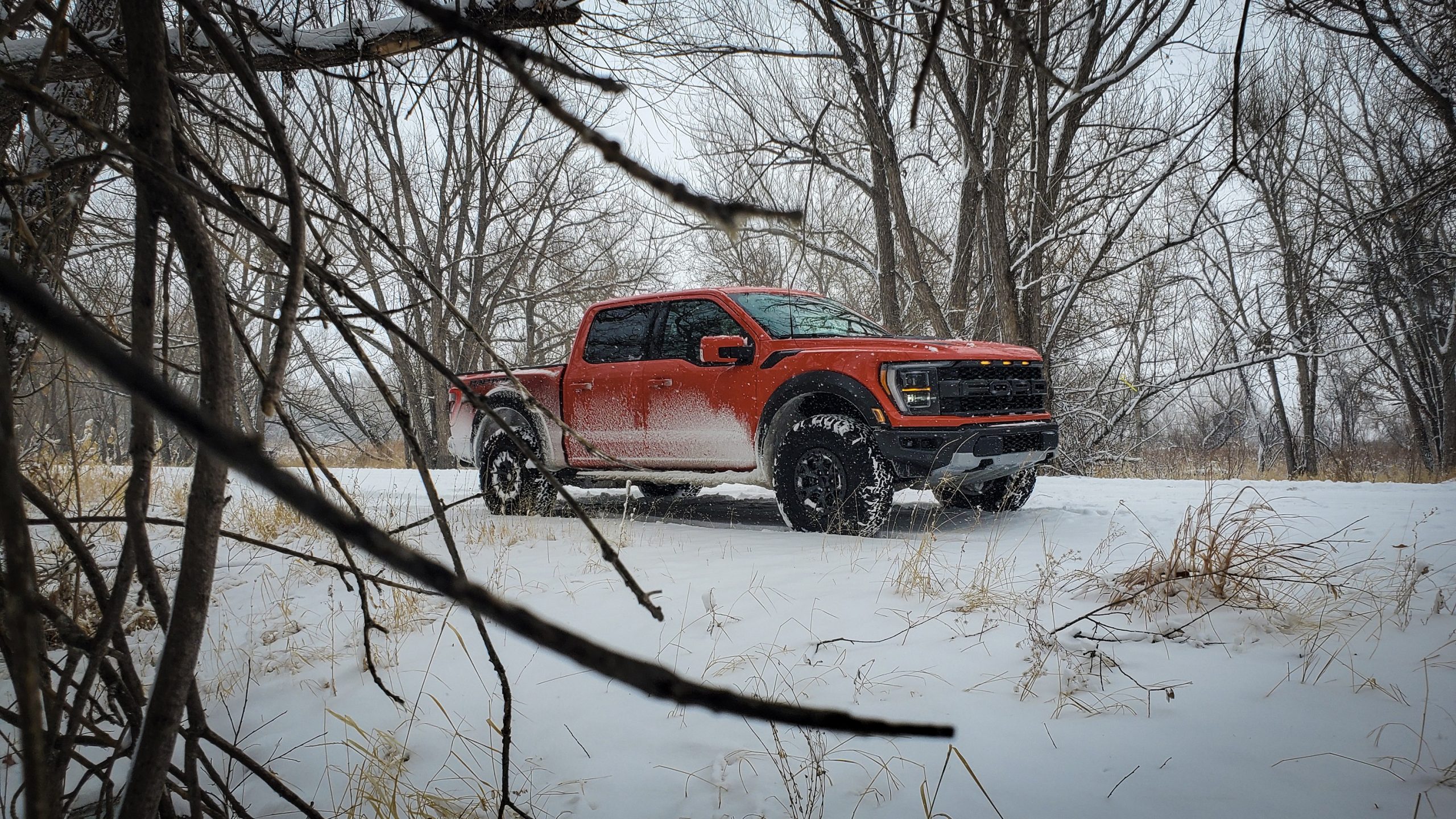 A 3/4 shot through the trees of the 2021 Ford Raptor 37 in orange