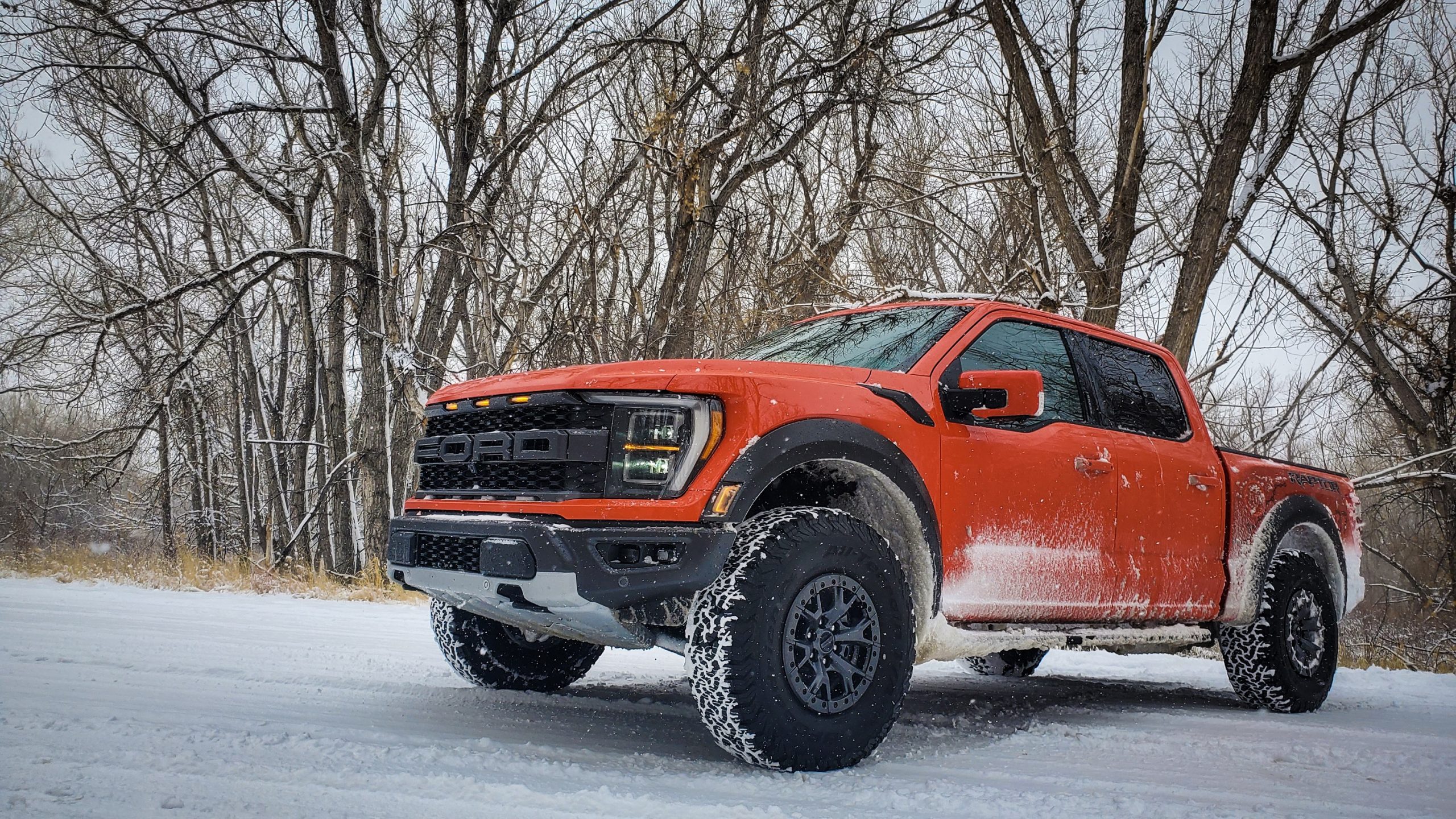 An orange F-150 shot from the front 3/4 during a snow storm