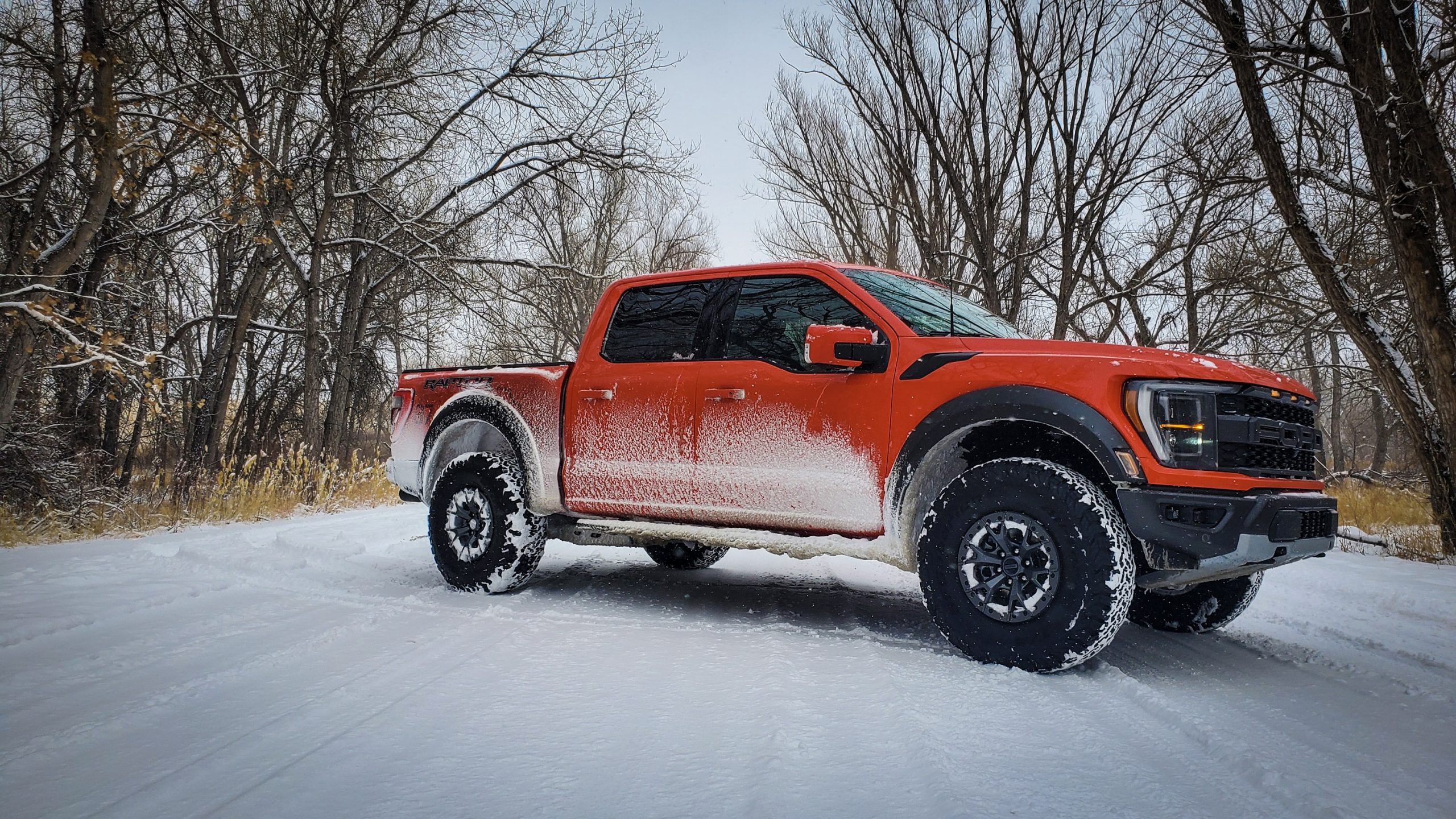 A 3/4 shot of the 2021 Ford Raptor truck in orange during a snowstorm