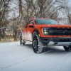 An orange 2021 Ford Raptor truck shot from the front 3/4 during a snow storm
