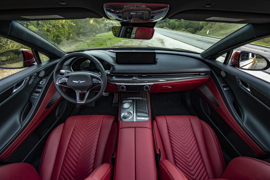 The red-leather front seats and wood-trimmed black dashboard of a 2022 Genesis G80 3.5T AWD Sport Prestige