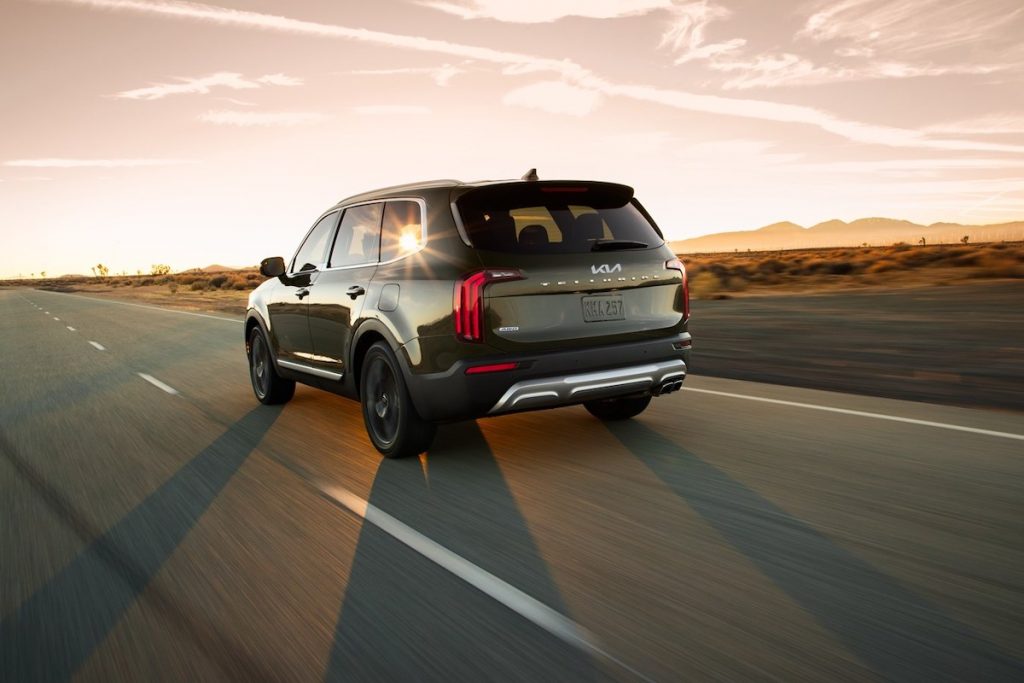 A dark-green 2022 Kia Telluride travels on a two-lane highway through a desert at sunset